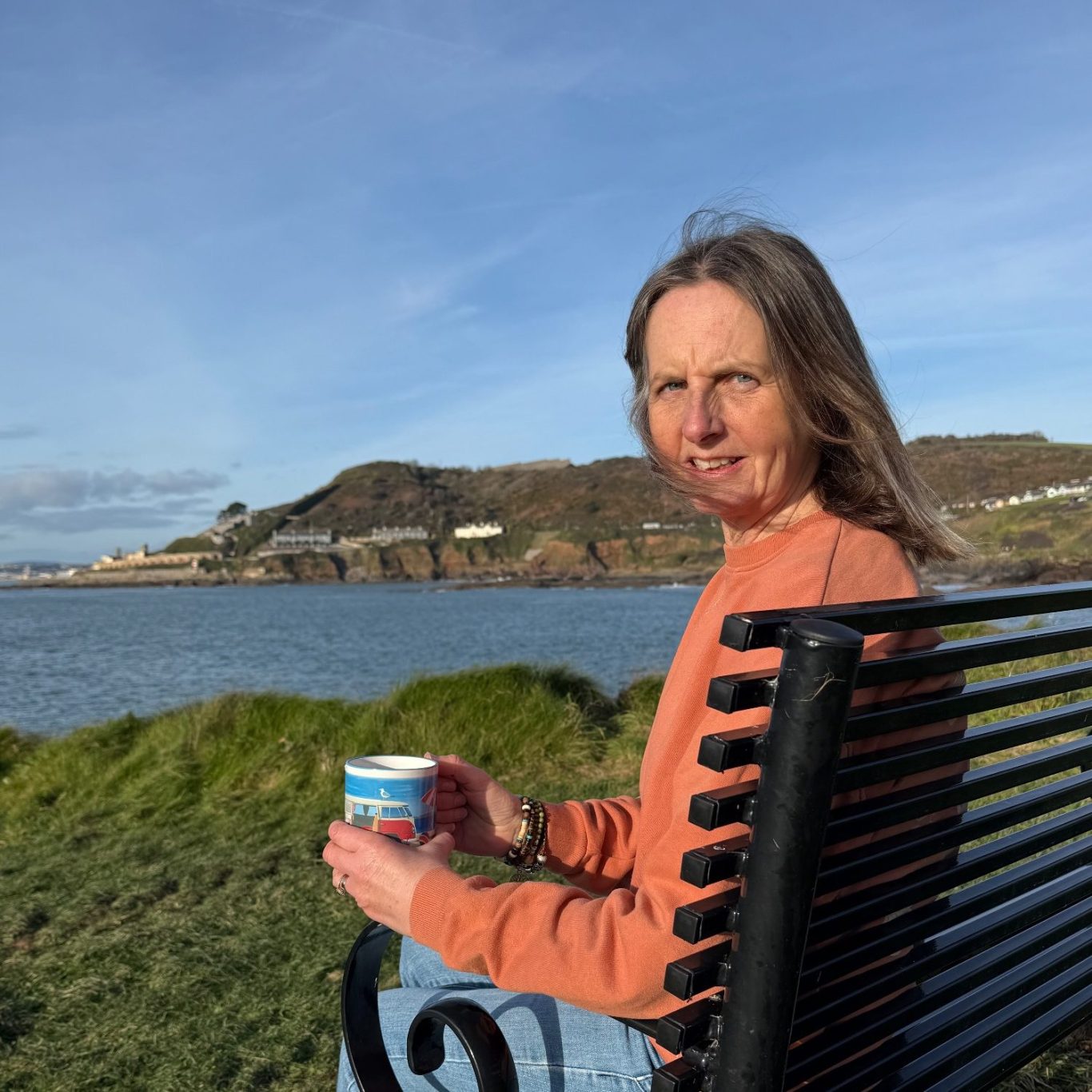 Jayne sitting on a bench enjoying views out to sea